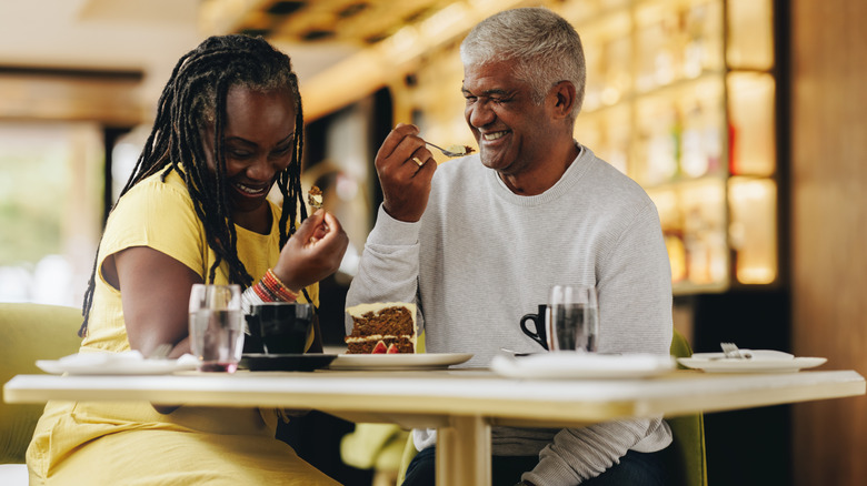 Older couple sharing a slice of cake at a restaurant and laughing