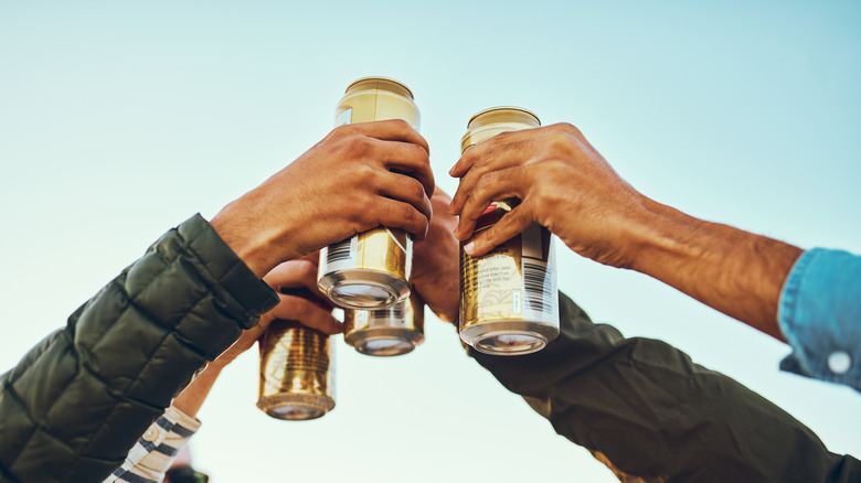 Cans of beer held aloft by several hands