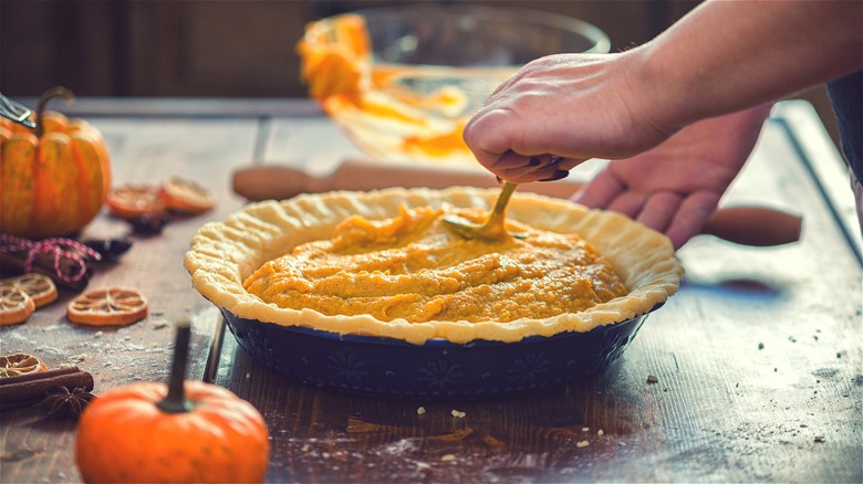 Hand adding pumpkin filling to pie