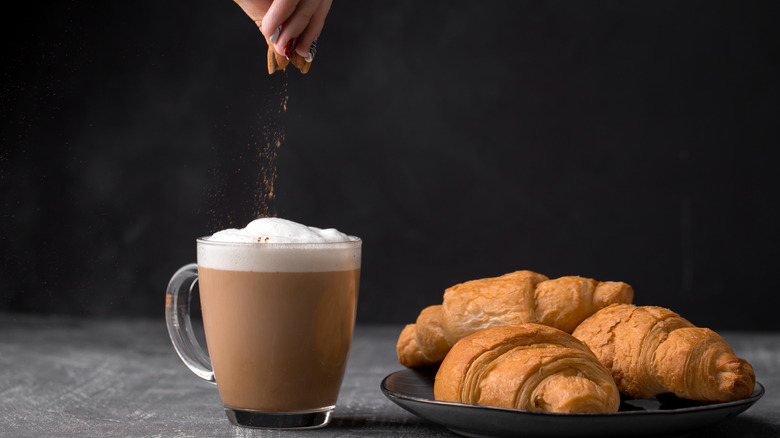 A person adds cinnamon to a coffee