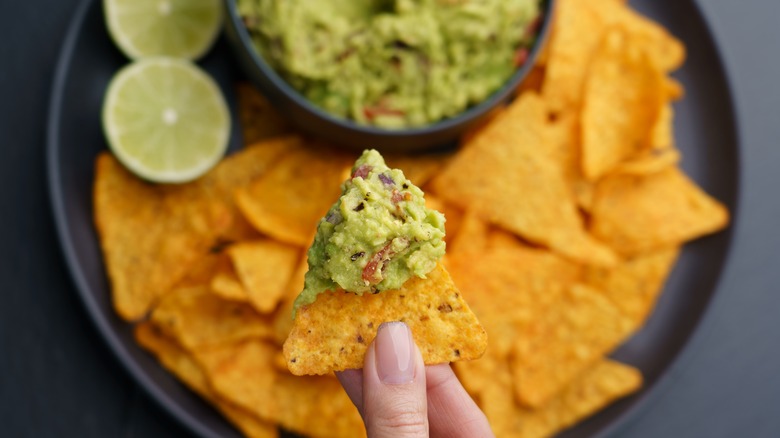 hand dipping chip in guacamole