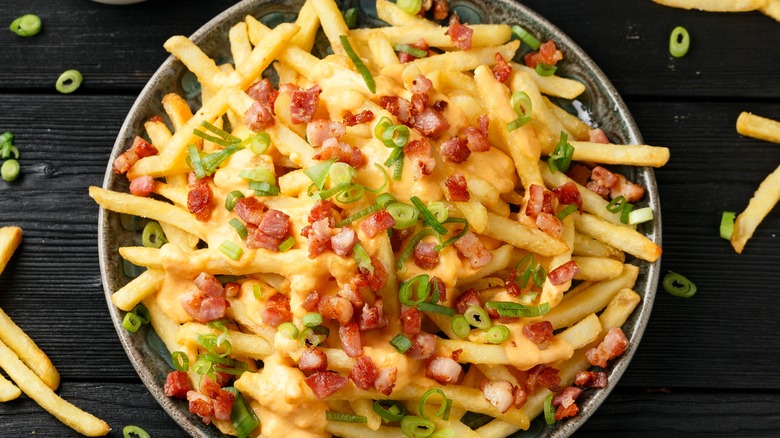 french fries in bowl with bacon and scallions on dark wood table