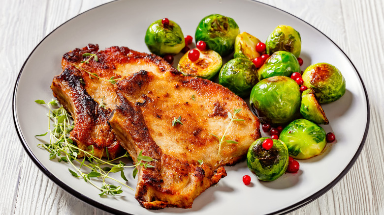 Pork chops, Brussel sprouts, and herbs on white plate