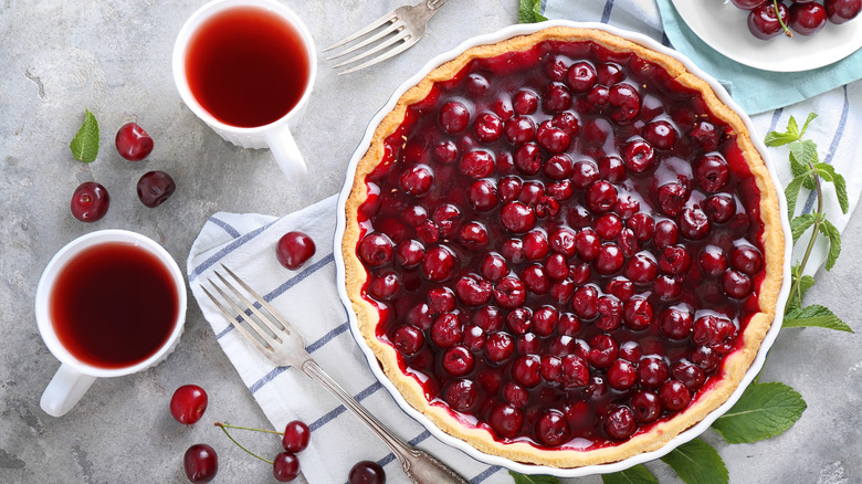 cherry pie on table with mugs of tea