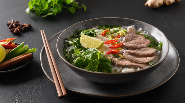 A bowl of pho on a plate with chopsticks