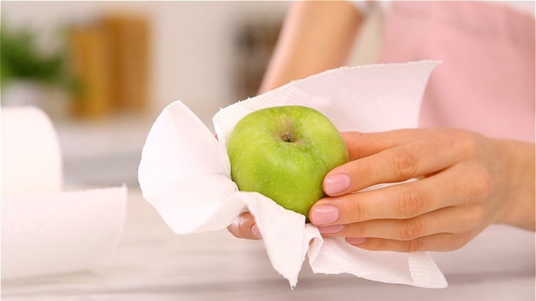 Hand wiping green apple with napkin