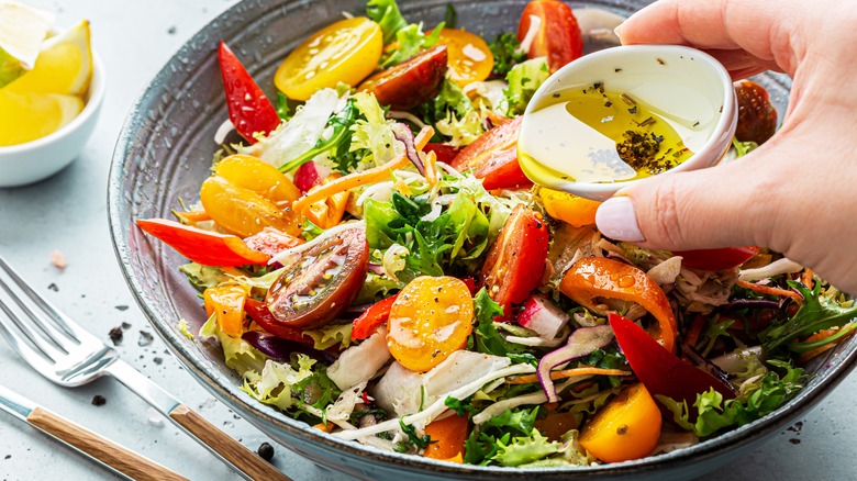 Hand pouring dressing on salad