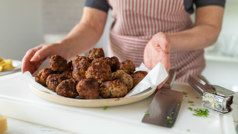 Woman holding sets of plain meatballs on kitchen counter