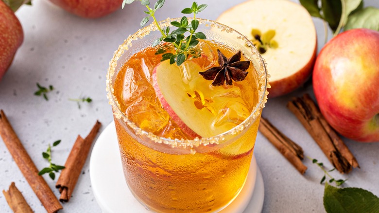 Glass of gold-colored beverage with sliced apple and anise