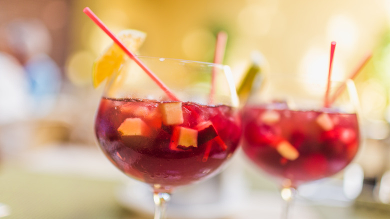 Two glasses of red sangria with fruit chunks and straws