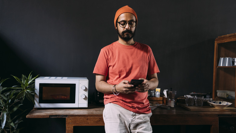 man on his phone in front of microwave