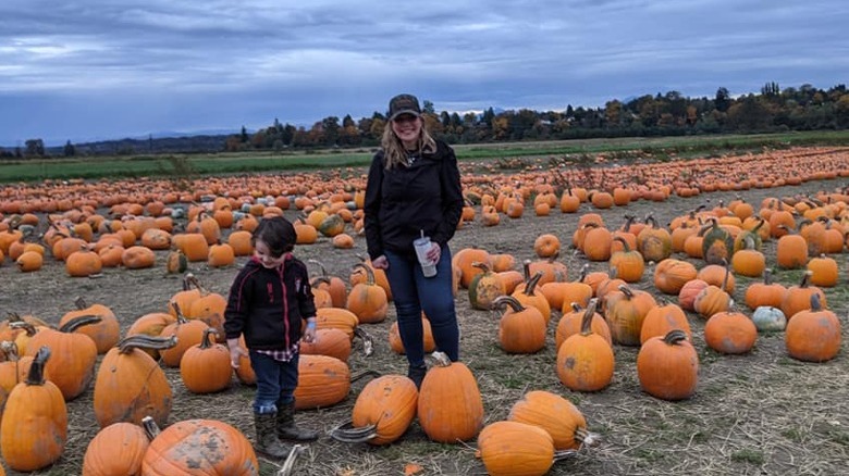 Woman, child standing among pumpkins