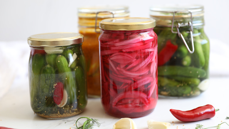 Pickled red onion in jar beside pickled vegetables