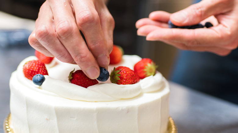 baker placing fresh strawberries and blueberries on cake