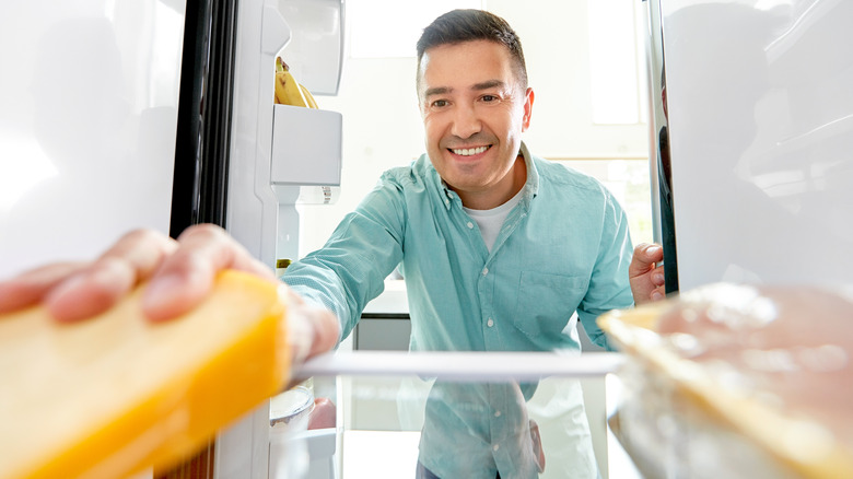 man placing cheese in fridge