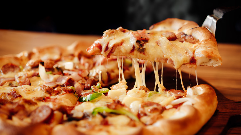 Pizza slice being lifted from whole pie