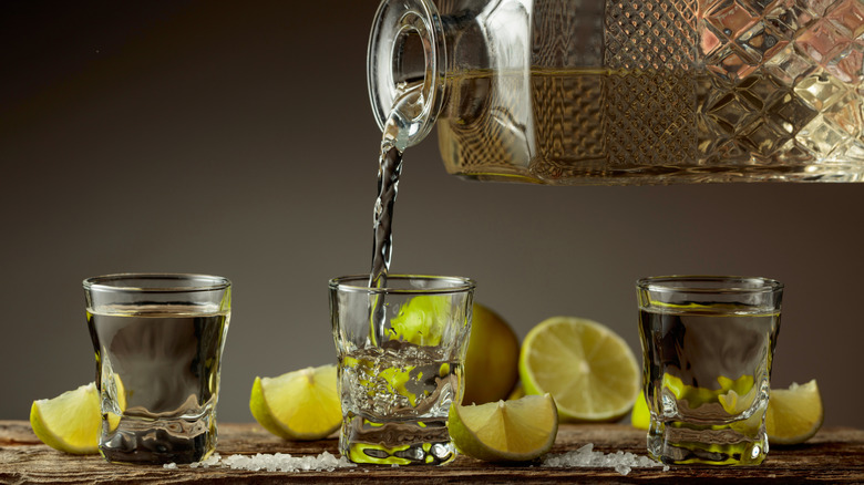 Pouring tequila into glasses from decanter with lime and salt