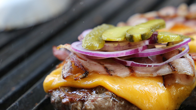 close up burger on grill with melted cheese purple onion pickle