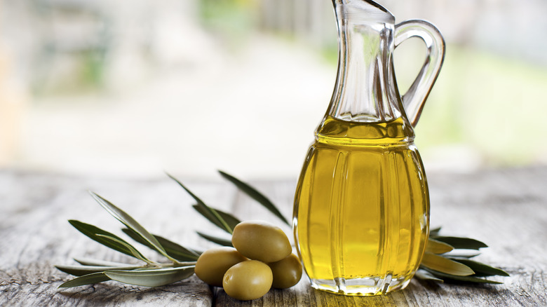 Glass jug of olive oil and olive branches