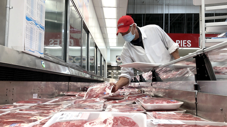 A Costco employee adjusting a display of meat