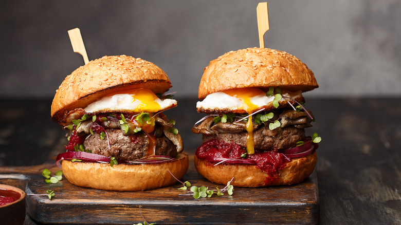 Two burgers with fried eggs on wooden board