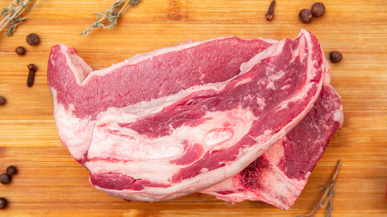 Beef steaks sitting on wooden board, with herbs and spices sitting around them