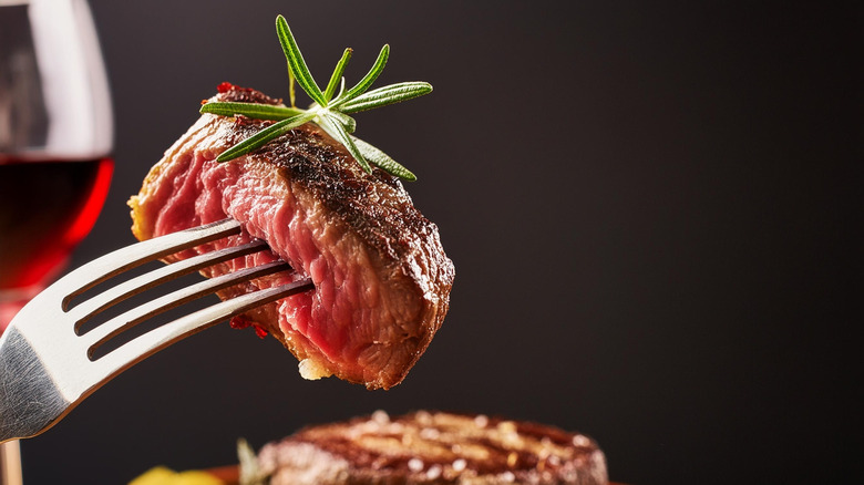 Piece of rare steak held up on fork, with sprig of rosemary on top