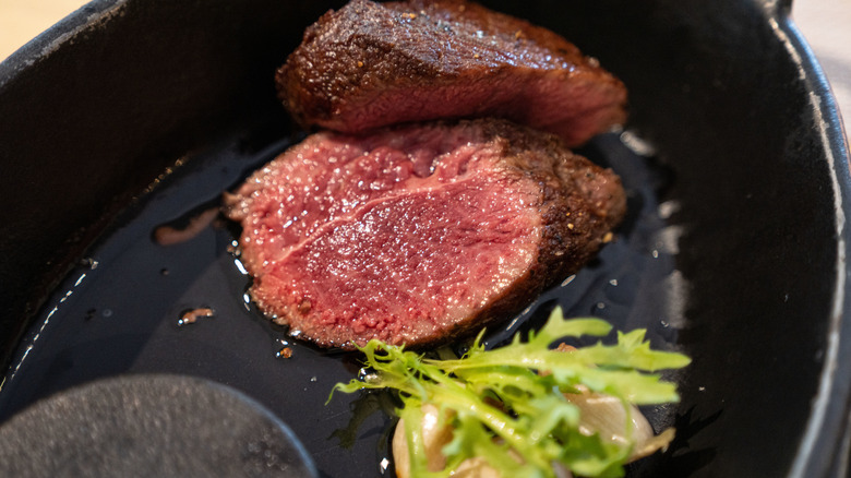 Blue steak in skillet, with sprig of salad greens