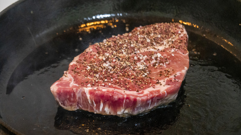 Steak cooking in pan, with seasoning sprinkled on top