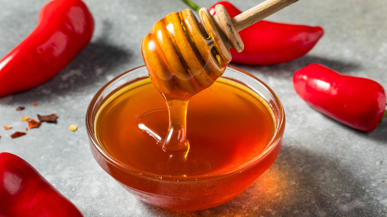 Bowl of hot honey surrounded by chilies, with honey dipper drizzling honey into the bowl