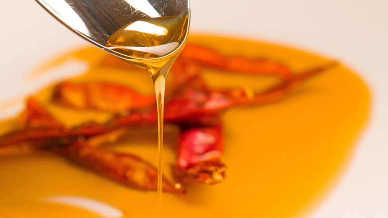 Honey dripping off spoon, with chilies in the background