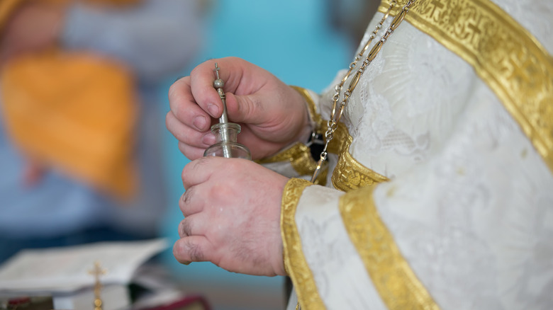 priest's hands holding glass bottle 