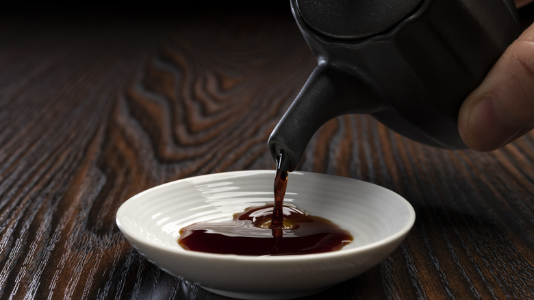 shoyu being poured from a ceramic jug onto a small plate