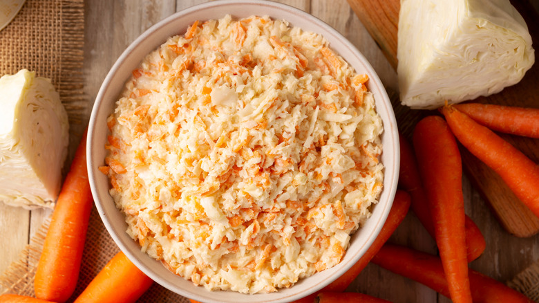 Bowl of fresh coleslaw, with cabbages and carrots surrounding it