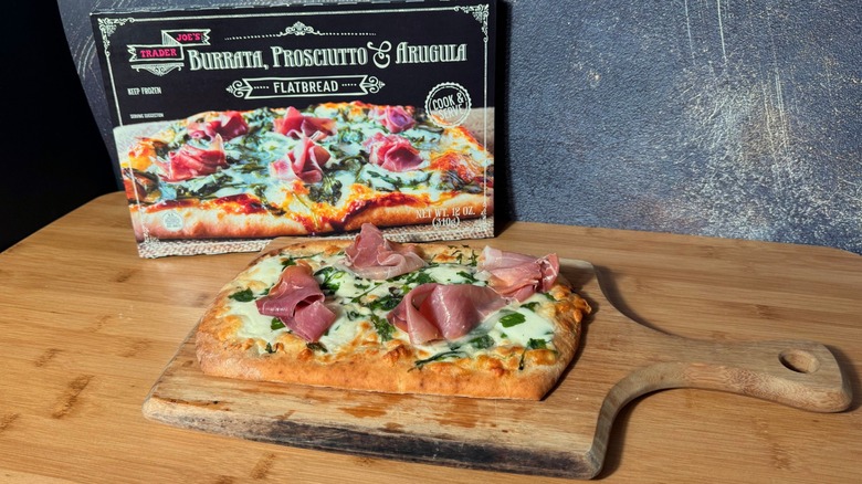 Flatbread with pieces of fresh prosciutto, on a wooden board next to its box