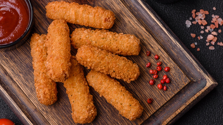 A set of mozzarella sticks next to marinara dipping sauce on dark background