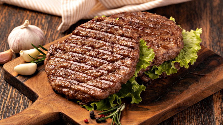 Burger patties with lettuce and garlic on a serving board