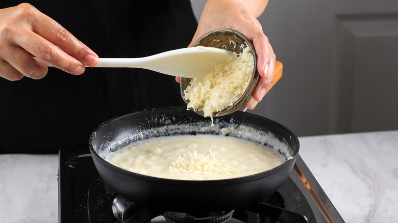 Cook adding grated cheese to a bechamel sauce