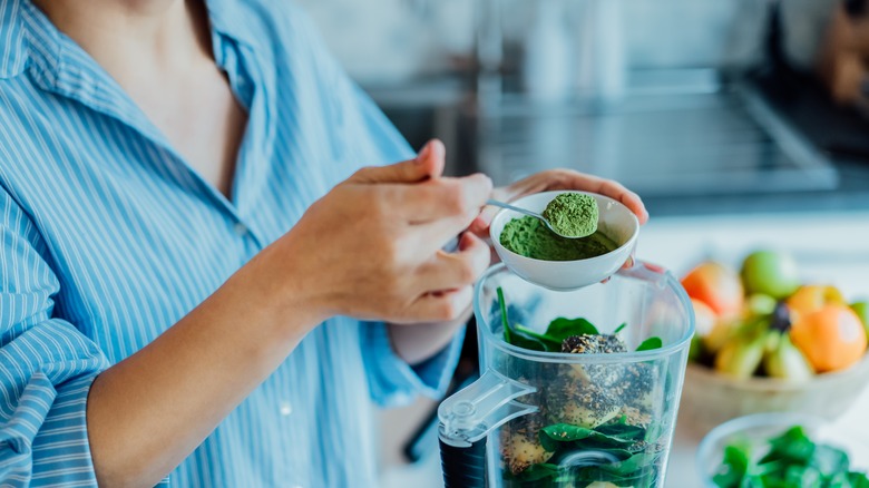 A woman adds matcha to her blender