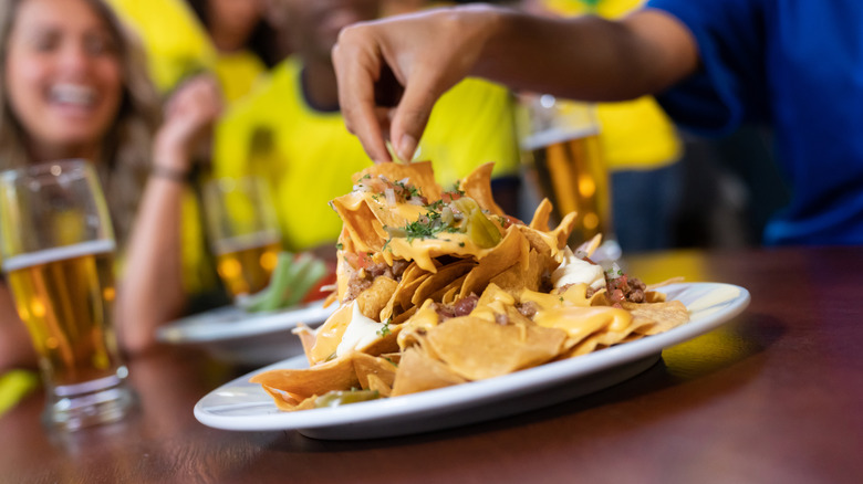 person pulling from plate of nachos