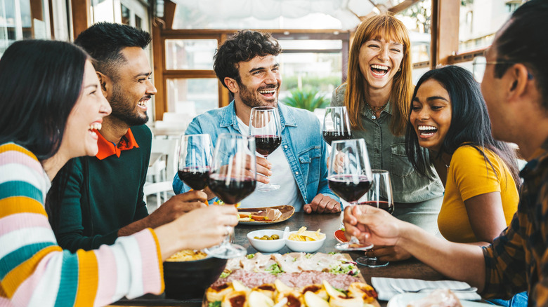 Group of people drinking wine and laughing with food at a table.