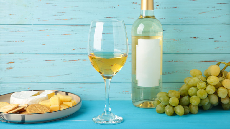 Glass and bottle of white wine sit beside cheese and cracker platter.