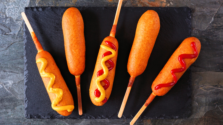 Corn dogs with ketchup and mustard on black slate