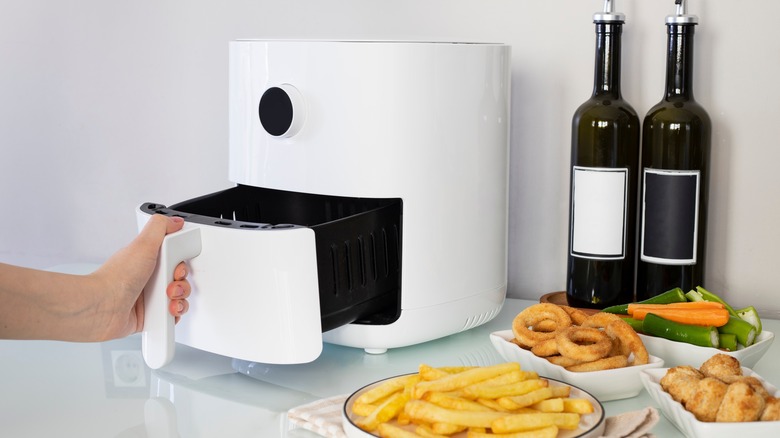 hand opening air fryer next to plates of food