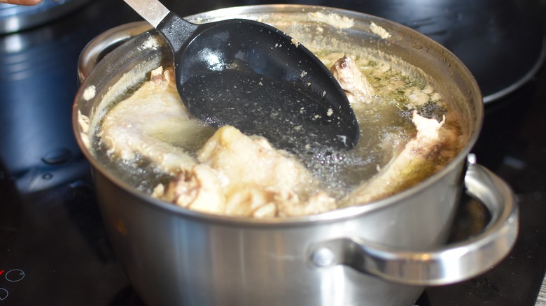 Person skimming foam from chicken broth