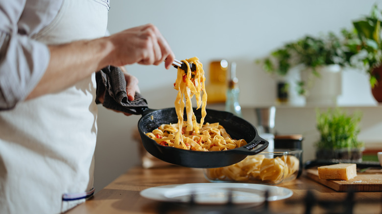 Chef plates pasta from a skillet