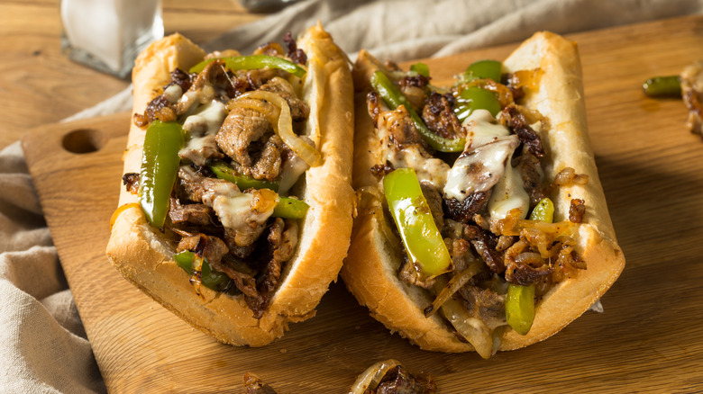 Homemade Philly cheesesteak sandwiches resting on a wooden serving board