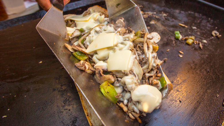 Philly cheesesteak filling being placed into toasted hoagie roll