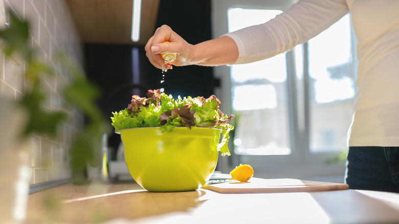 person squeezing lemon juice on salad in yellow bowl