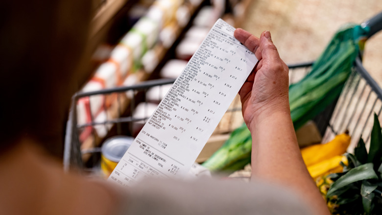 Person holding receipt over cart of groceries